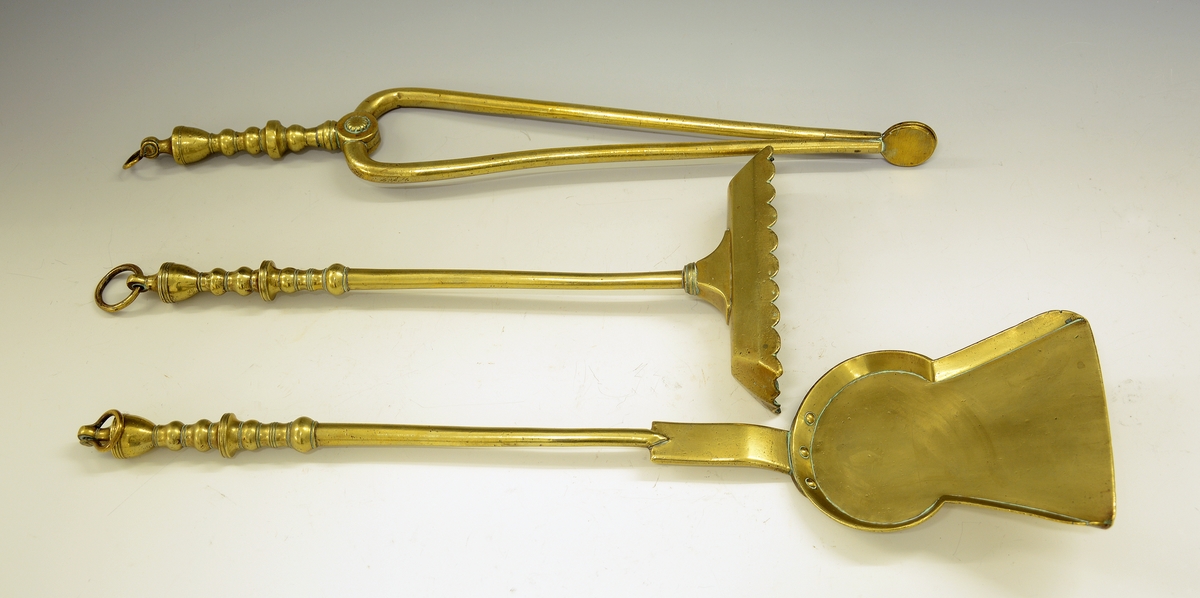 Ildtang av messing, del av peissett i tre deler. Bøyle øverst til oppheng, dreide kuler og blomst der armene deler seg. Avslutning på armene er to ovaler.