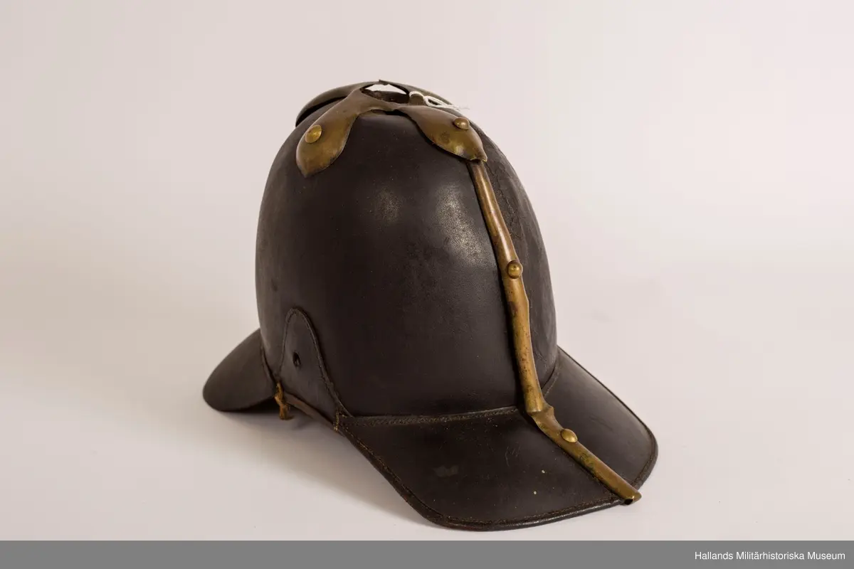 En s.k kask (hjälm) av svart styvt läder. Hjälmen är svagt sluttande upptill med förgylld plåt. Hjälmen har fram- och bakskärm. Förgylld plåt på baksidan som löper lodrätt från toppen av hjälmen ner på bakskärmen. Brunt läder på insidan.