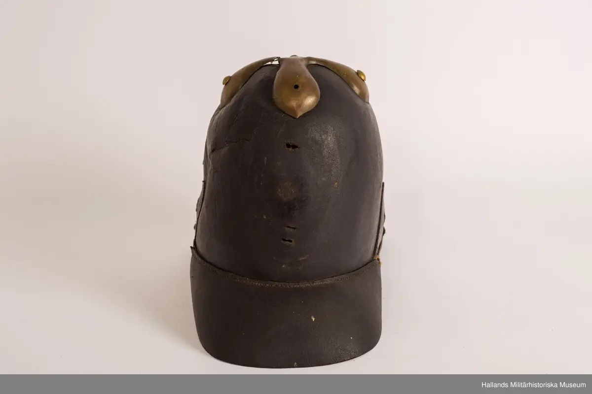 En s.k kask (hjälm) av svart styvt läder. Hjälmen är svagt sluttande upptill med förgylld plåt. Hjälmen har fram- och bakskärm. Förgylld plåt på baksidan som löper lodrätt från toppen av hjälmen ner på bakskärmen. Brunt läder på insidan.