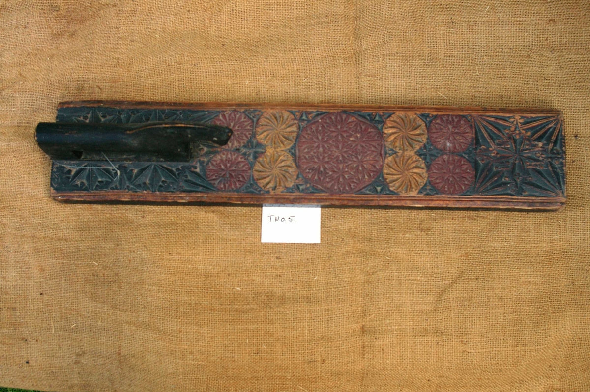 Mangletreet er malt sort, rødt og gull. Karveskur, med store og små seksbladsroser og buestjerner. Inskripsjon: anno 1743, dato 26 februar. Nils Øistensøn Marsta. Hestehåndtak.