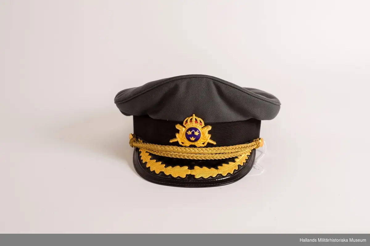 En skärmmössa för officer i stålgrått tyg. Mössan har svartlackerad skärm och mörkt stålgrått mössband kring stommen. Mössrem för generalpersoner och regementsbefäl, tillverkad i tjock flätad guldtråd. Mössremen är fäst i två små knappar ( guld m/1767) på vardera sidan av mössan. Knapparna bär Generalstabens emblem (två korslagda kanoner). Mössmärke till skärmmössa m/60, för officer på framsidan av mössan samt skärmbroderi för generalsperson vilken betecknas med en eklövskrans. Svart botten inuti, tillverkarens etikett på botten samt ägarens namnlapp.