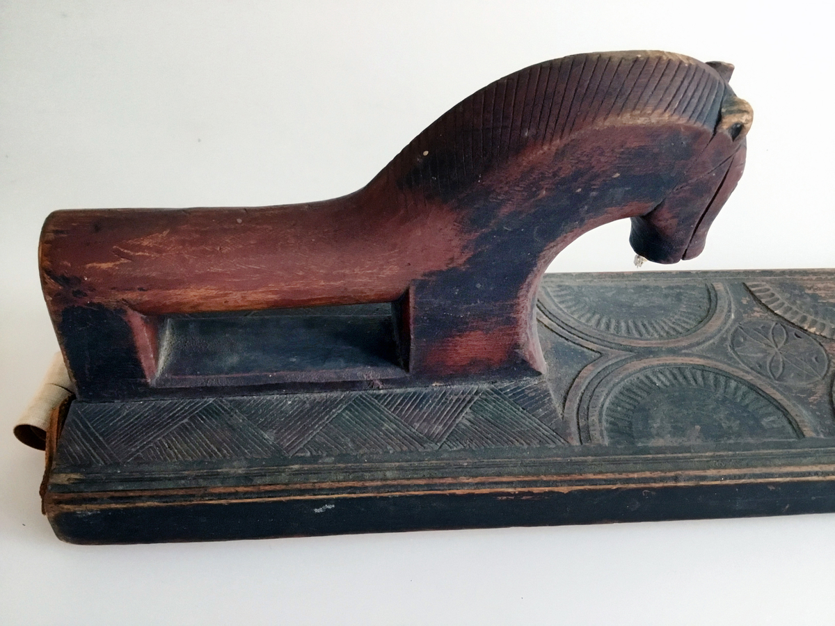 Mangletreet er malt rødt og sort. Karveskurd. Hestehåndtak, smal profil på sidene. Sikk sakk ornamentikk ved hestehåndtaket. Dekorert med sirkler og halvsirkler, og seksbladsroser i sirklene. Lærhempe i enden. Håndtaket festet med jernskruer.