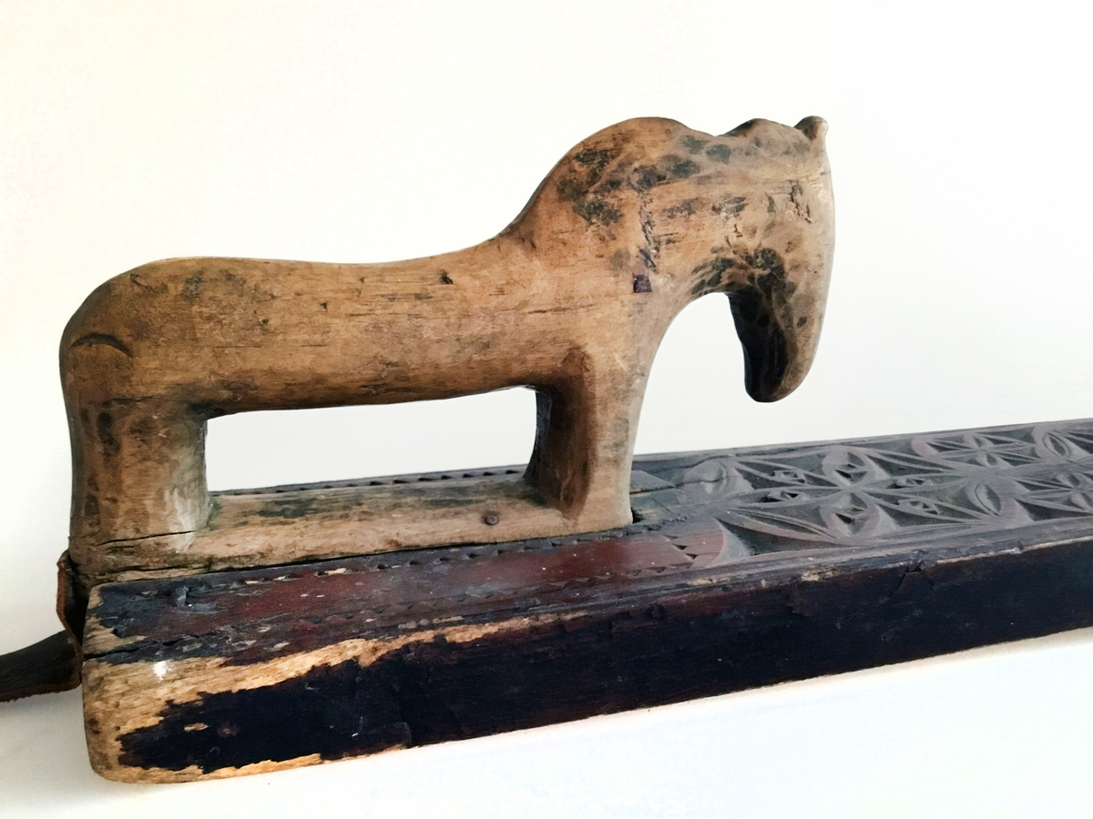 Mangletreet er malt rødt med to gule rosetter. Dekortert med store og små rosetter med seksbladsroser, og sikksakkbord ved håndtaket. Hestehåndtak. Datert 1804. Håndtaket er nyere og trefarget. Lærhempe i enden.