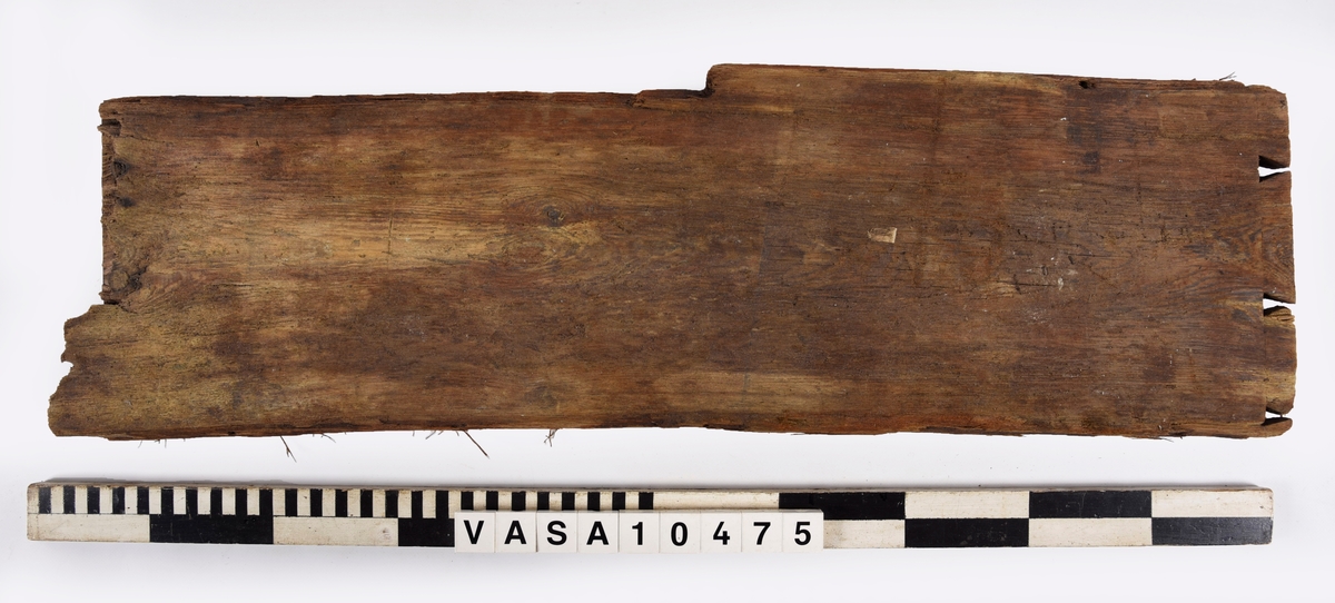 Fragment till en rektangulär bräda med väl bevarade laxstjärt stycken på ena ände. En avbruten sink på den andra ände. 2 spikhål med huvudspår längs en långkant.
det Original föremålet var dubbelt längd - avbruten längs sinket. Avbrytningar och kraftig vittring på långkanter.