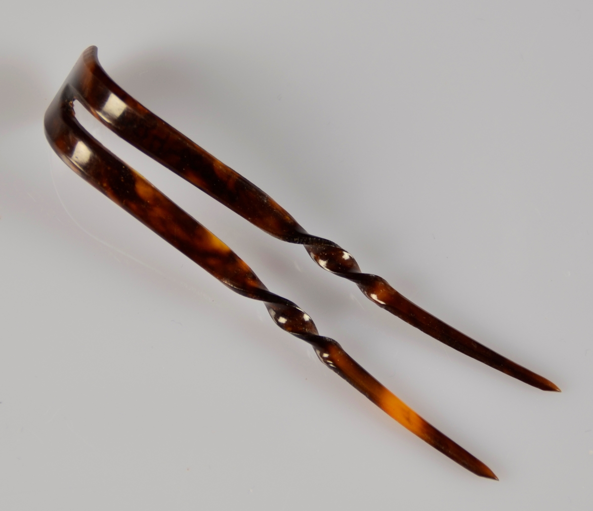 Hårnål til hårtopp i brun, truleg, plast. Brunfargen med spettar med lysare farge. U-form der enda bogar oppover, med lange, rette bein der midten er vridd i spiral.