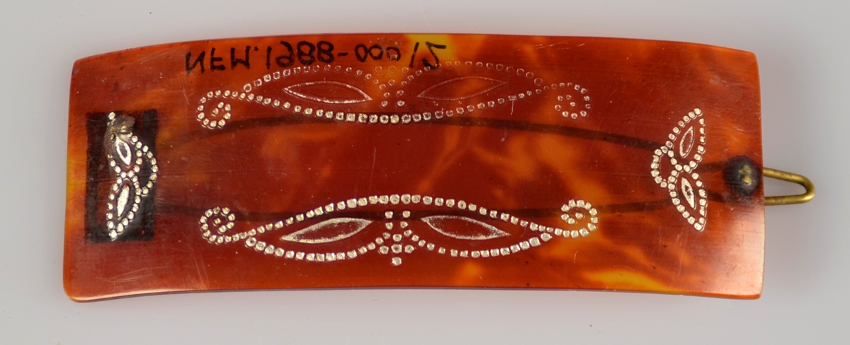 Hårspenne i brunt, marmorert, gjennomskineleg materiale med sølvfarga dekor og metall klype på bakside.