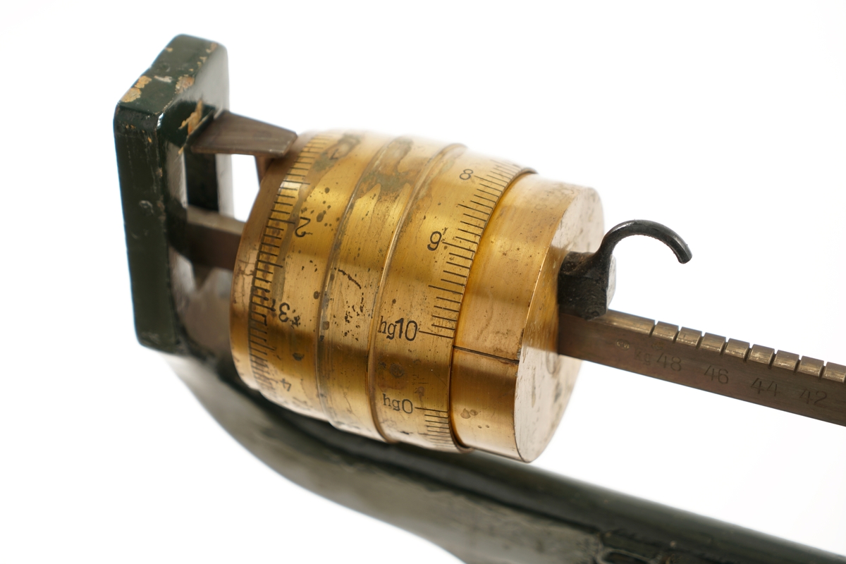 Balansevekt av metall bestående av fot,ben,vektarm og vektskål.