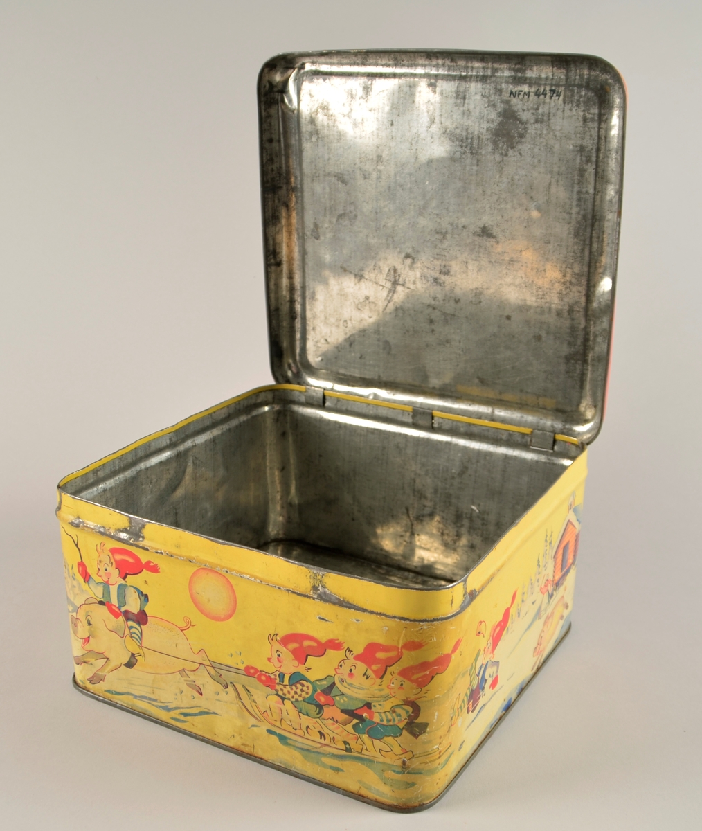 Boks med hengsla lok. Jarnblikk. Trykk på sidene på gul bakgrunn. Motiv er nisser på slede dradd av griser.