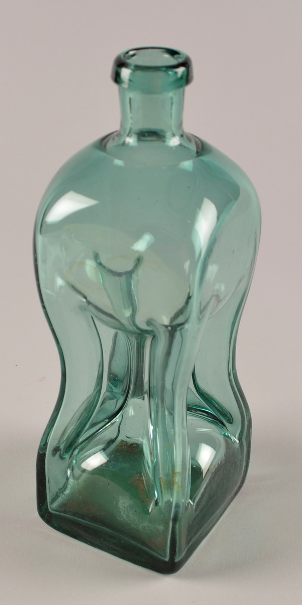 Flaske i lys grønt glas. Fire sider, der det er "knipe" inn midt på sida i kvart hjørne, slik at det vert fire smale røyr i kvart hjørne og i mdoten av flaska som væska i flaska renn gjennom ved skjenking. Likesida.