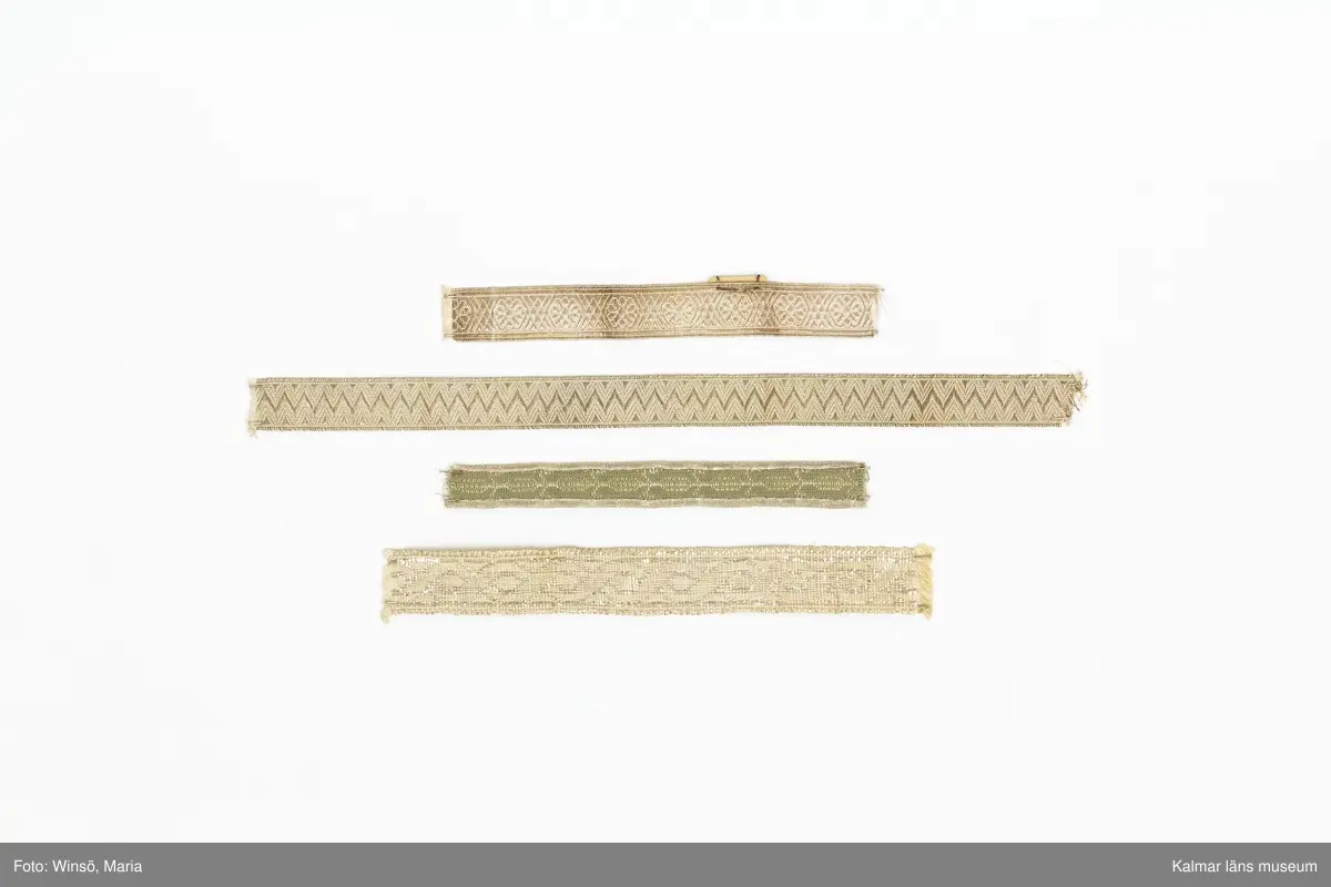 KLM 28082:184:2:1-15. Silverband, 15 stycken, av bomull och metall, silver, varierande mönster, längd och bredd. 6 olika sorters band. :1-5 Band, silvergalon, 5 stycken, silver, mönsterbård, silverblomma, sex linjer, korsande varandra och bildar en romb, mellan blommorna. (jmf. provkarta på KLM 28082:184:1:1-2). :5 Band med etikett i kartong, med siffrorna 3,25 i blyerts. :6 Band, silver, med triangelmönster. :7-14 Band, 8 stycken, baksida, helt i silver, framsida, med invävd bomullstråd, mönsterbård och silverkant. :15 Band, med bred sivertråd. Framsida, mönsterbård, åttor, som bildar lång fläta. Baksida, helt i silver. Etikett av papper runt bandet med nummer och längd, skrivna i bläck och blyerts.