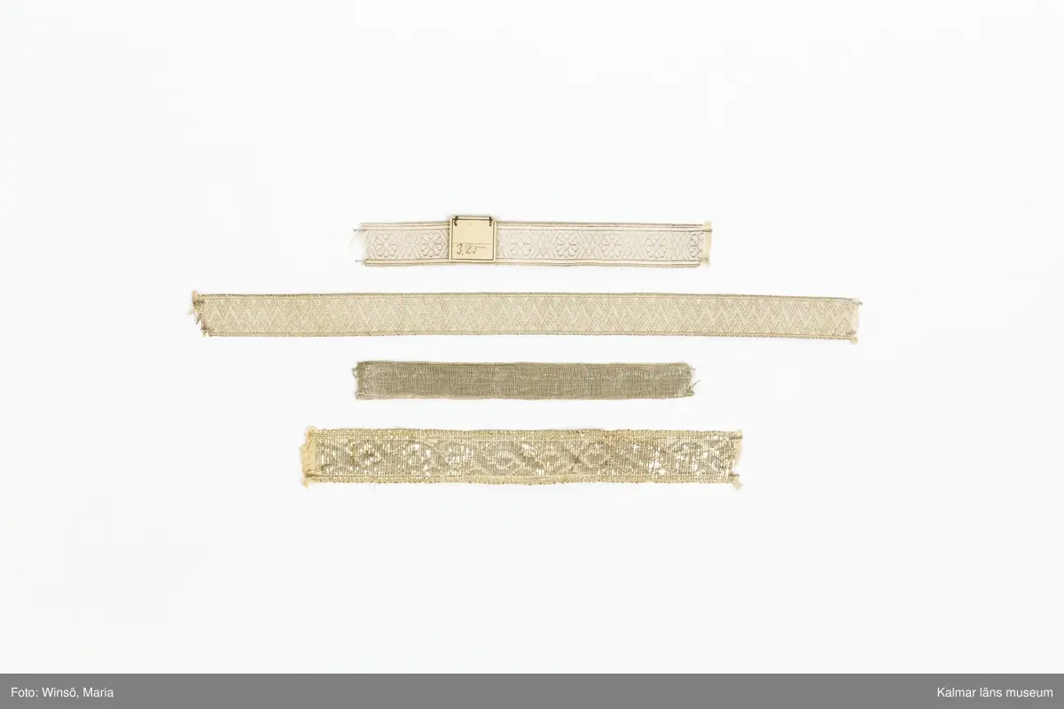 KLM 28082:184:2:1-15. Silverband, 15 stycken, av bomull och metall, silver, varierande mönster, längd och bredd. 6 olika sorters band. :1-5 Band, silvergalon, 5 stycken, silver, mönsterbård, silverblomma, sex linjer, korsande varandra och bildar en romb, mellan blommorna. (jmf. provkarta på KLM 28082:184:1:1-2). :5 Band med etikett i kartong, med siffrorna 3,25 i blyerts. :6 Band, silver, med triangelmönster. :7-14 Band, 8 stycken, baksida, helt i silver, framsida, med invävd bomullstråd, mönsterbård och silverkant. :15 Band, med bred sivertråd. Framsida, mönsterbård, åttor, som bildar lång fläta. Baksida, helt i silver. Etikett av papper runt bandet med nummer och längd, skrivna i bläck och blyerts.