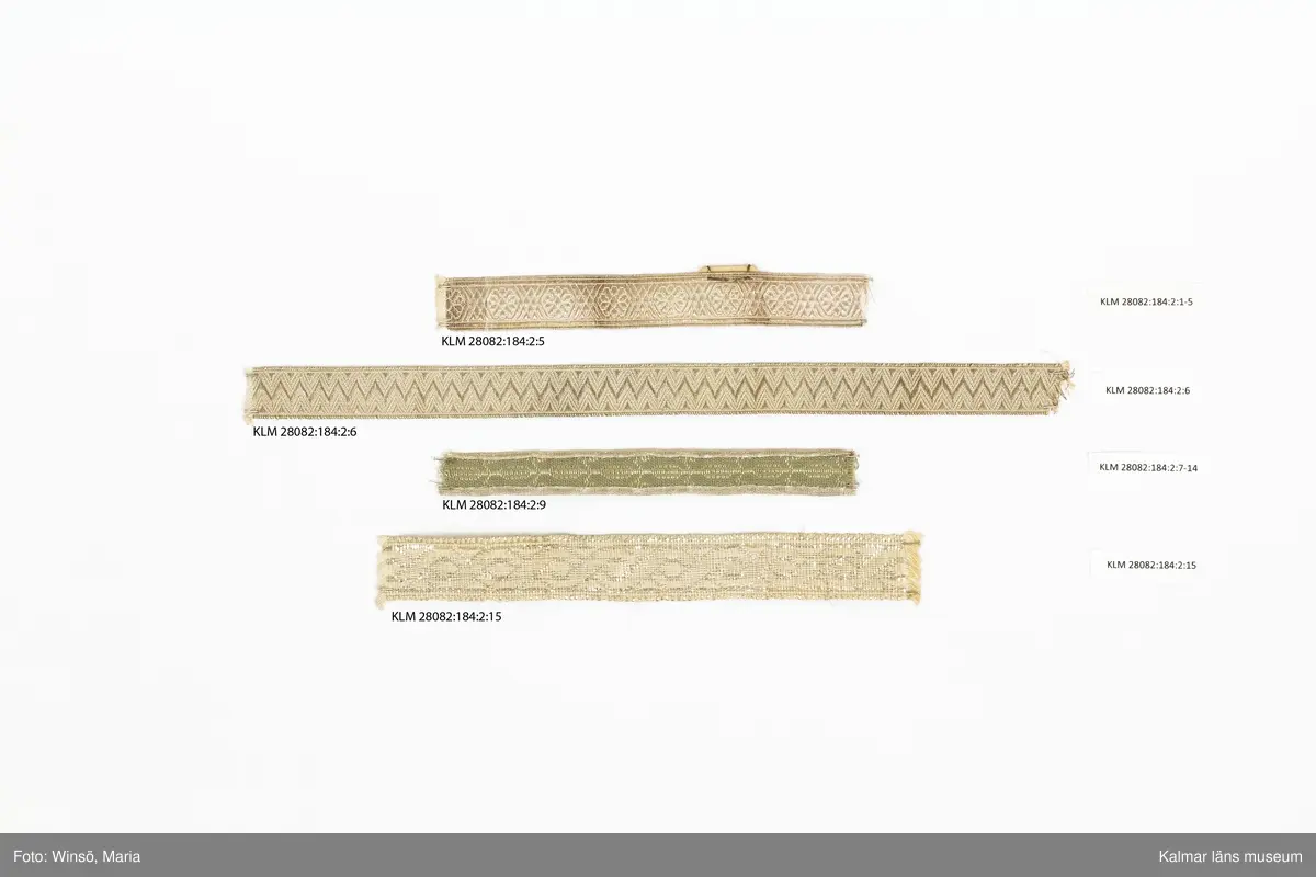 KLM 28082:184:2:1-15. Silverband, 15 stycken, av bomull och metall, silver, varierande mönster, längd och bredd. 6 olika sorters band. :1-5 Band, silvergalon, 5 stycken, silver, mönsterbård, silverblomma, sex linjer, korsande varandra och bildar en romb, mellan blommorna. (jmf. provkarta på KLM 28082:184:1:1-2). :5 Band med etikett i kartong, med siffrorna 3,25 i blyerts. :6 Band, silver, med triangelmönster. :7-14 Band, 8 stycken, baksida, helt i silver, framsida, med invävd bomullstråd, mönsterbård och silverkant. :15 Band, med bred sivertråd. Framsida, mönsterbård, åttor, som bildar lång fläta. Baksida, helt i silver. Etikett av papper runt bandet med nummer och längd, skrivna i bläck och blyerts.