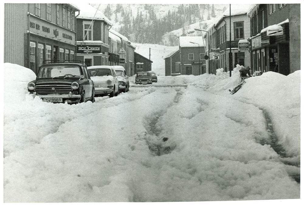 En vårdag med snø og parkerte biler i Peter Bechs gate. Nærmeste bil XV-11003: Bilskilt med to bokstaver og fem siffer fra 1.  mai 1971.  Morris 1100 ca. 1970-modell.