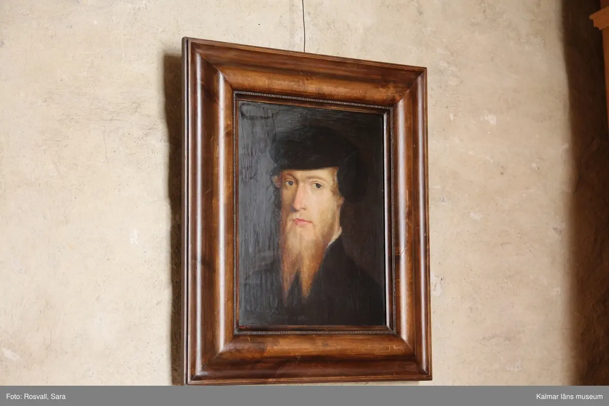 Erik XIV avbildad i bröstbild, face vänster, med svart rock med liten vit spetskrage som precis skymtar och svart barett. Tudelat skägg. Umbrafärgad bakgrund.