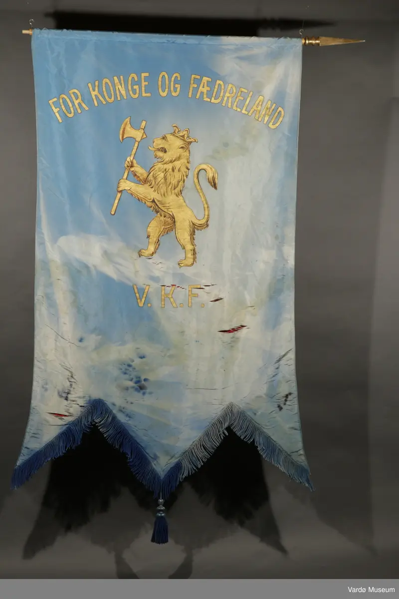 Lyseblå fane. Øverst står det "For konge og fædreland", under er løven fra riksvåpenet malt i gull, og helt nederst på fanen står initialene "V. K. F.". Baksiden er rød.