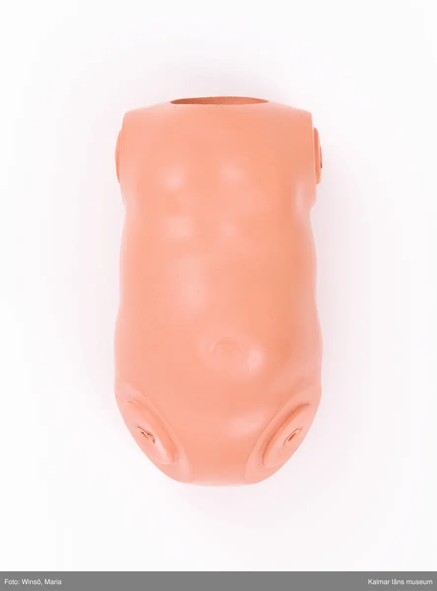 KLM 28082:224 Docka, del av, dockkropp, av celluloid, hudfärgad. Hål, (diameter ½ cm), ett för vardera dockarm som saknas, hålen är sammankopplade genom ett plaströr, ett likadant plaströr för dockben som även de saknas. Dockkropp tillverkad genom pressning och består av två hopfogade delar. I nacken sköldpaddsmärke i en romb, och 49. Tillverkad av, Schildkröt-Puppen und Spielwaren GmbH, Tyskland.