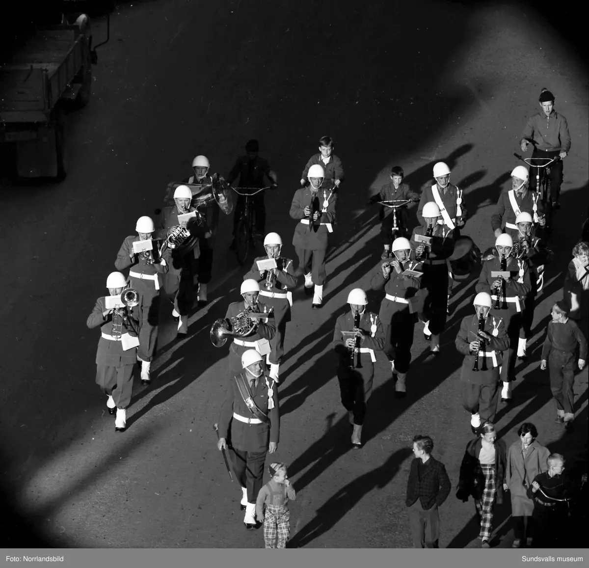 En stor serie bilder från firandet av Svenska flaggans dag 1956. Parad på Storbron med paradorkester, militär, scouter och mängder av olika föreningar och förbund. Därefter högtidlig uppställning i Idrottsparken med bland annat tal, körsång, gymnastikuppvisning och folkmusik.