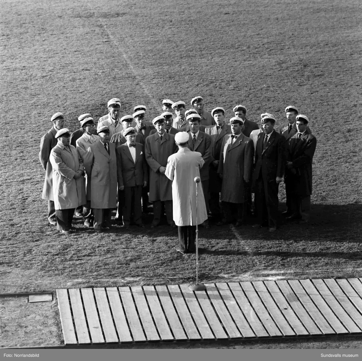 En stor serie bilder från firandet av Svenska flaggans dag 1956. Parad på Storbron med paradorkester, militär, scouter och mängder av olika föreningar och förbund. Därefter högtidlig uppställning i Idrottsparken med bland annat tal, körsång, gymnastikuppvisning och folkmusik.