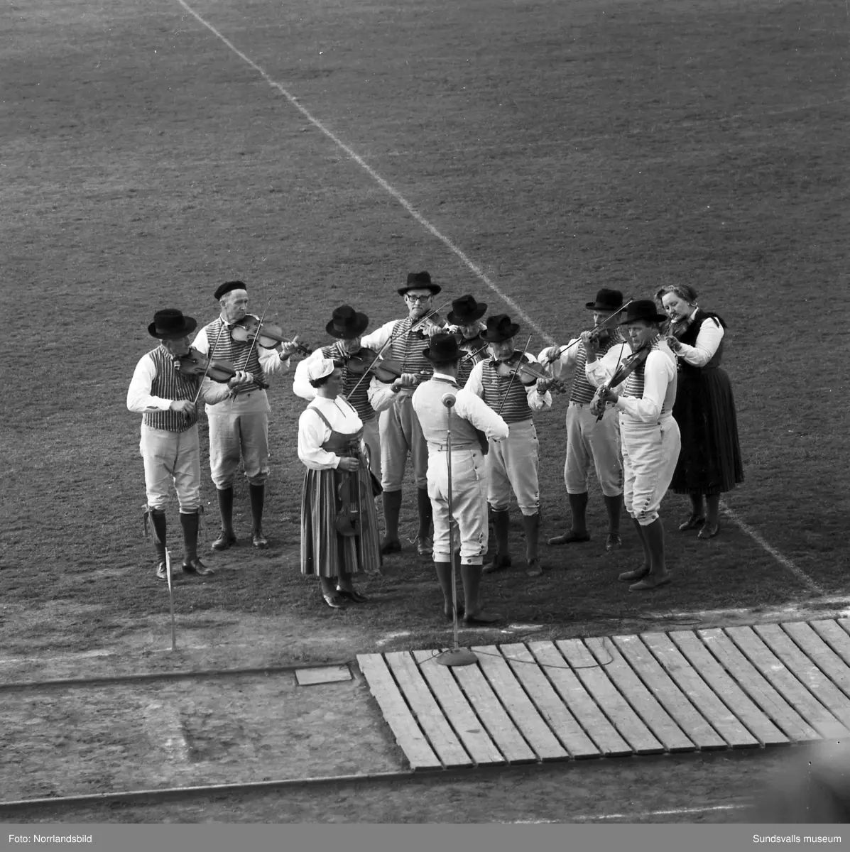 En stor serie bilder från firandet av Svenska flaggans dag 1956. Parad på Storbron med paradorkester, militär, scouter och mängder av olika föreningar och förbund. Därefter högtidlig uppställning i Idrottsparken med bland annat tal, körsång, gymnastikuppvisning och folkmusik.