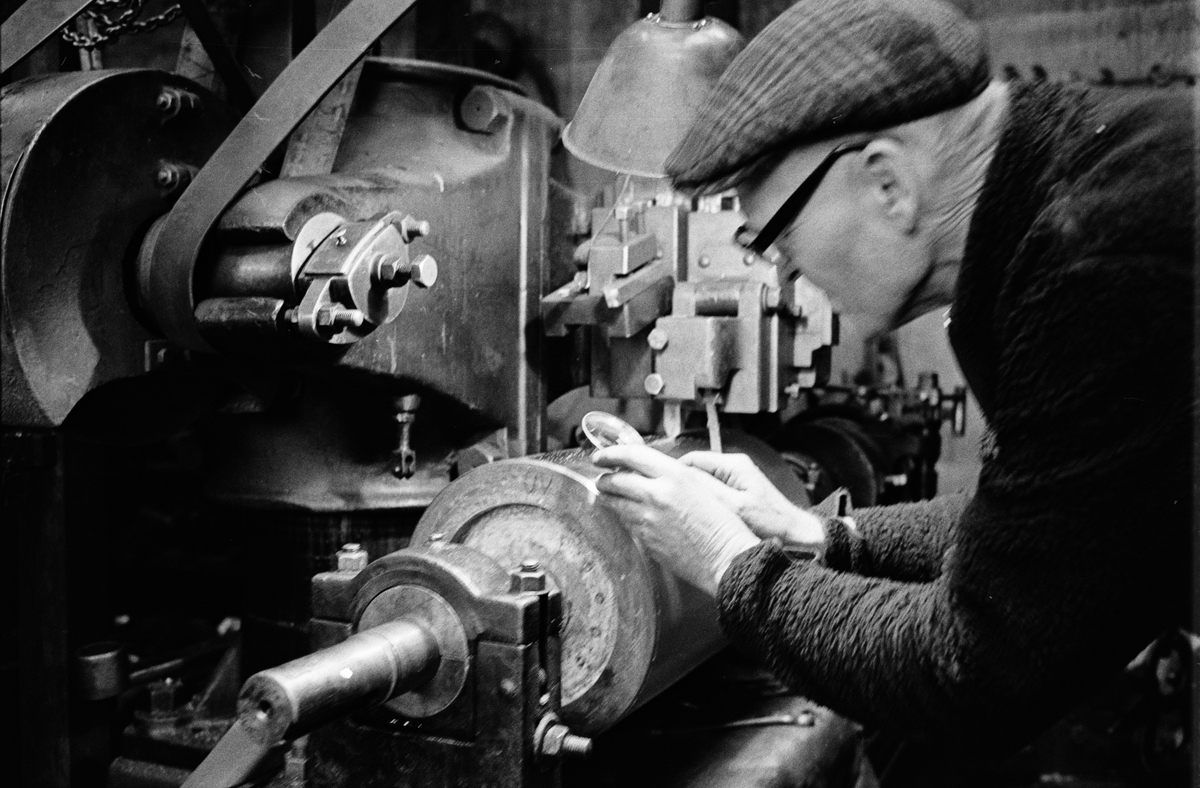 Fabrikör Karl-Gustav Johansson kontrollerar kvarnvalsens räfflor med hjälp av ett förstoringsglas, Enköpings Kvarnstensfabrik, Bangårdsgatan 13, Enköping, Uppland 1984