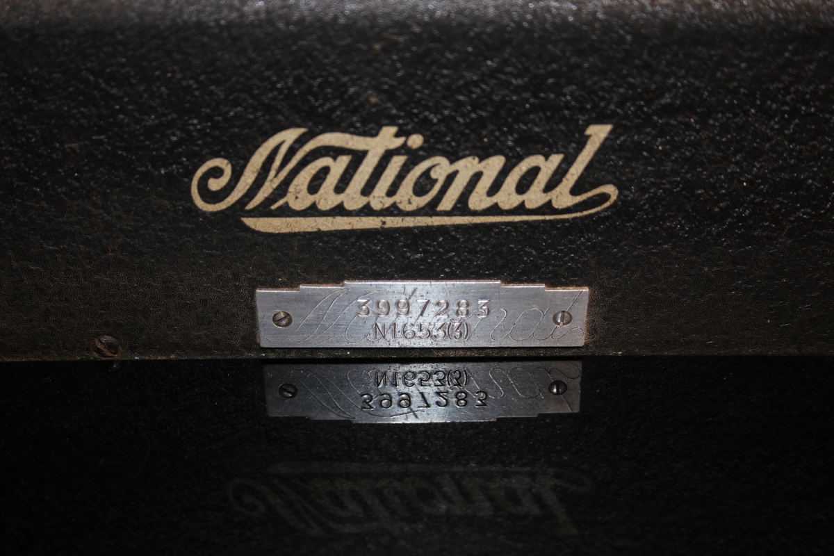 Kassa-apparat med sokkel, pengeskuff og sveiv, 5 skalaer for kr. og øre. Vindauga for kronesum framme og bak. 5 knottar. Nøkkel til skuff.