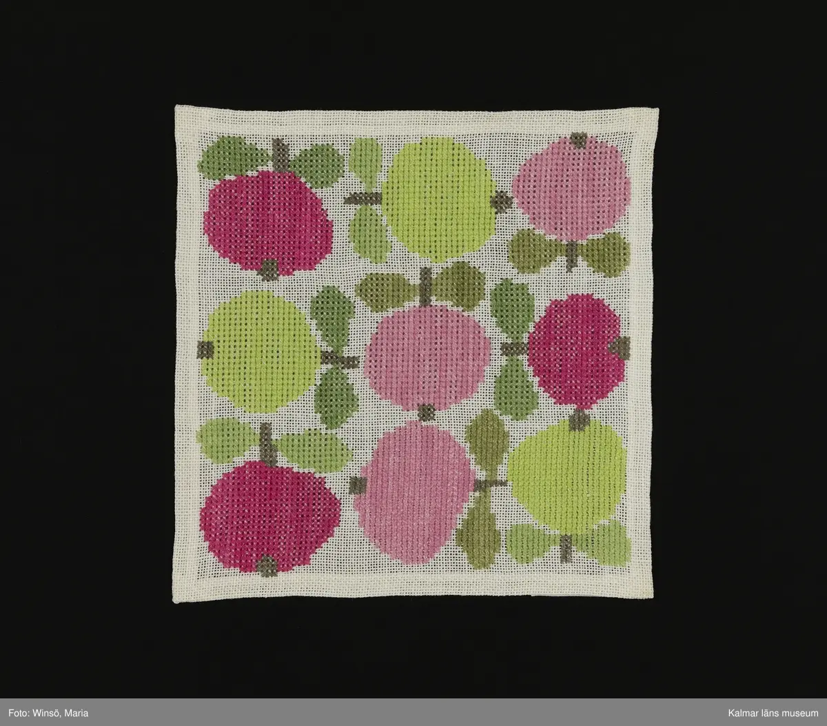 Äppen broderade åt olika håll på vit bakgrund i orange och rosa kulör, med gröna blad (:1) och i rosa och grön kulör med gröna blad (:2). Titel: "Äppelrutan".