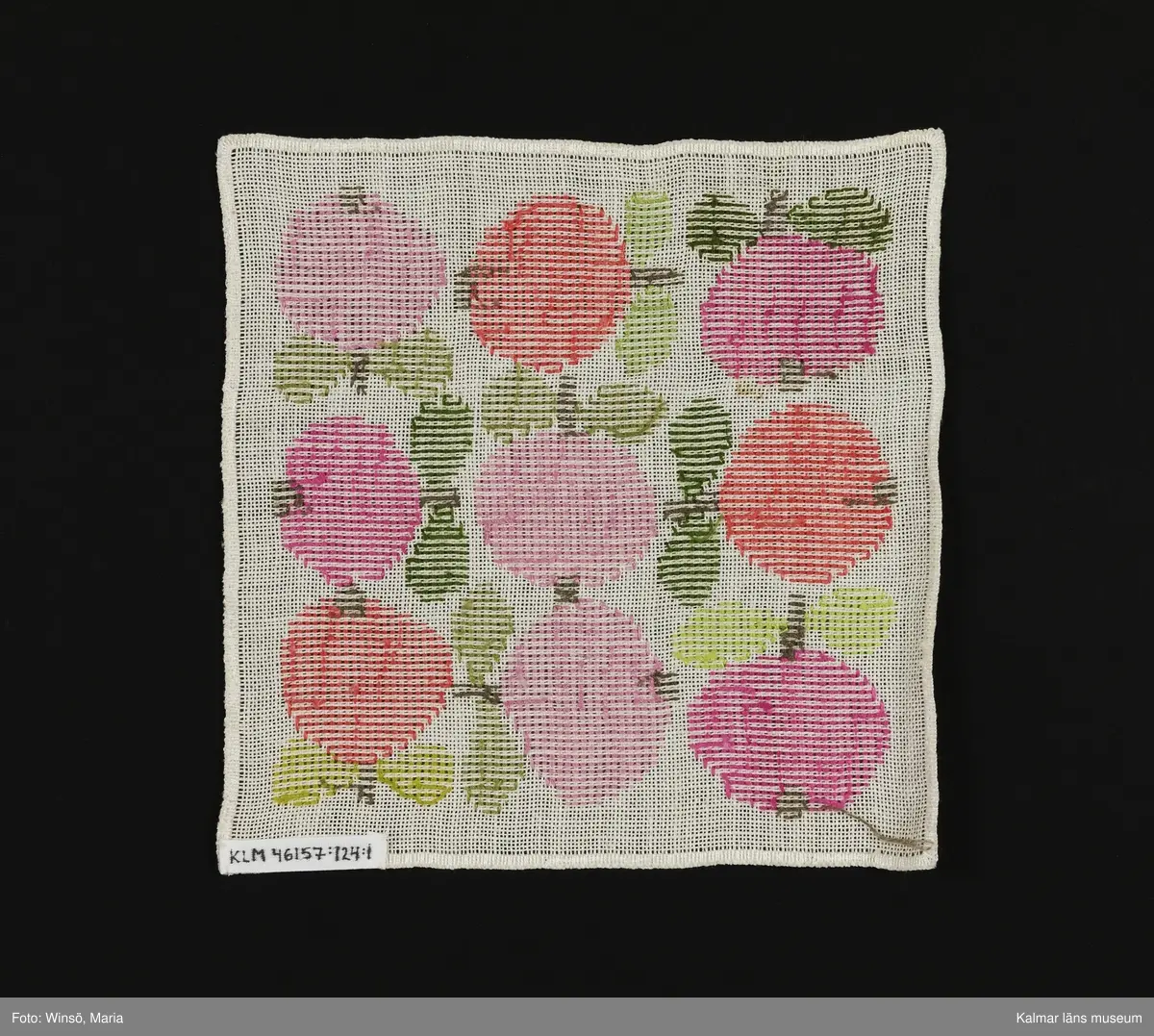 Äppen broderade åt olika håll på vit bakgrund i orange och rosa kulör, med gröna blad (:1) och i rosa och grön kulör med gröna blad (:2). Titel: "Äppelrutan".