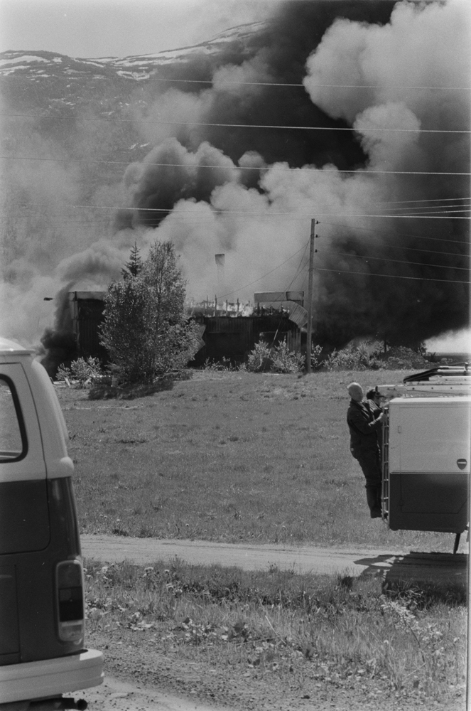 Båtfabrikken Polar-Industri A/S i Drevvatnet totalskadd ved brann 16 Juni 1978. Fabrikken brenner, mye røyk.
Brannbil med mann bakpå.