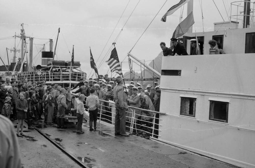 Sangere med amerikansk flagg ombord i båt ved Jernbanekaia.