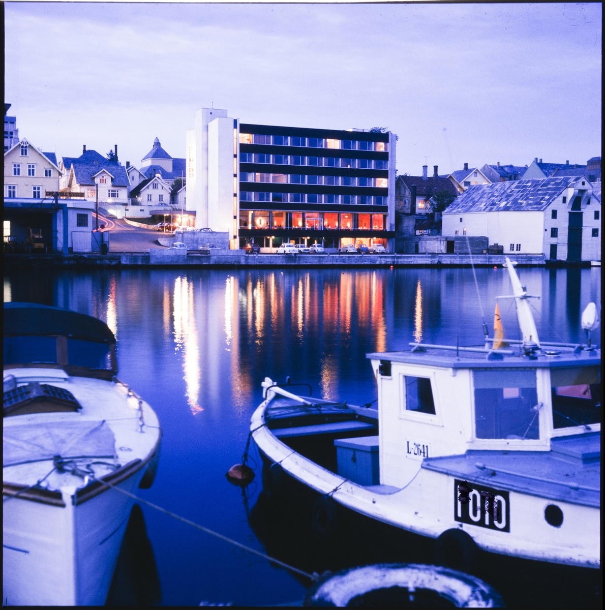 Hotel La Mer i Haugesund tatt over Smedasundet fra Risøy. Senere kjent som Hotell Maritim. Bildet er tatt i kveldslys. En fiskebåt ligger i forgrunnen.
