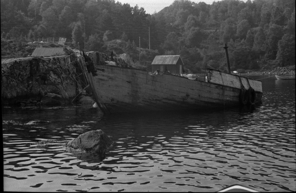 Vraket av fiskebåten M/S "Familien" ligger ved strandsonen i ei vik i Ålfjorden, Hordaland. Det er to hytter og et naust i nærheten.