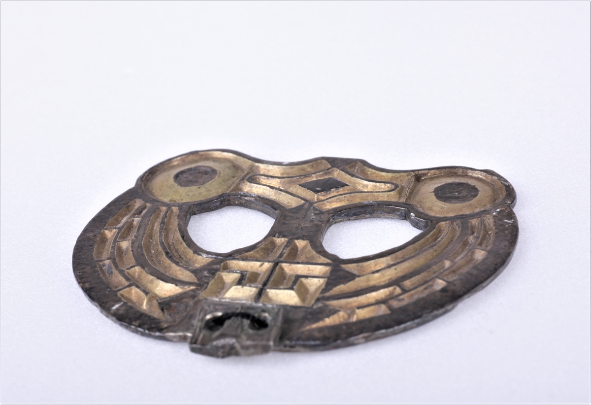 Sølvbeslag og en liten del av dens festeinnretning, forgylt med nielloinnlegg, som type R. 200 d fra eldre jernalder. Utsmykning til sverdslire. Funnet i en gravhaug på gården Mellom-Kvem.