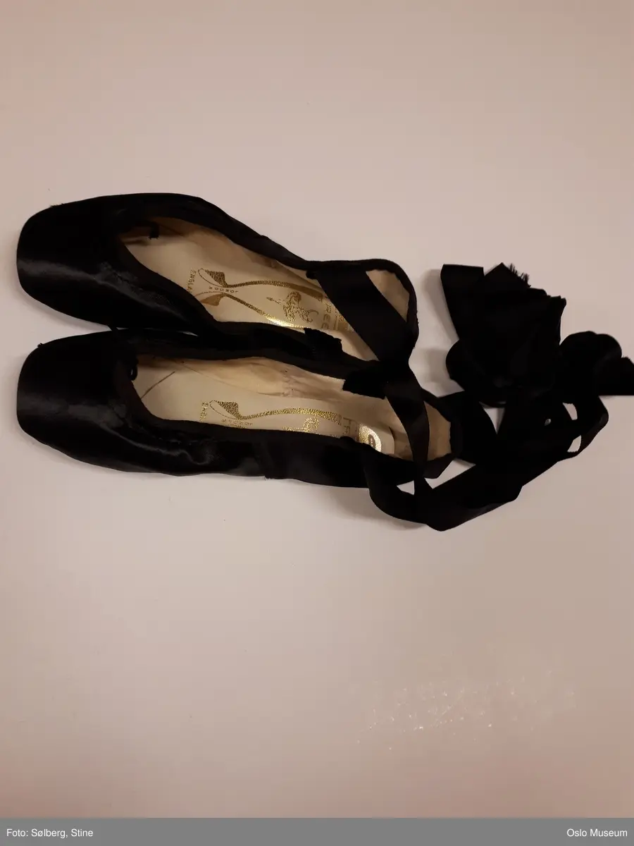 Halvlang rosa ballettkjole i silke med sorte blonder og to løse små ermer, samt et par svarte ballettsko med svarte bånd.
A: Kjole
B: Løst erme
C: Løst erme
D: Ballettsko
E: Ballettsko