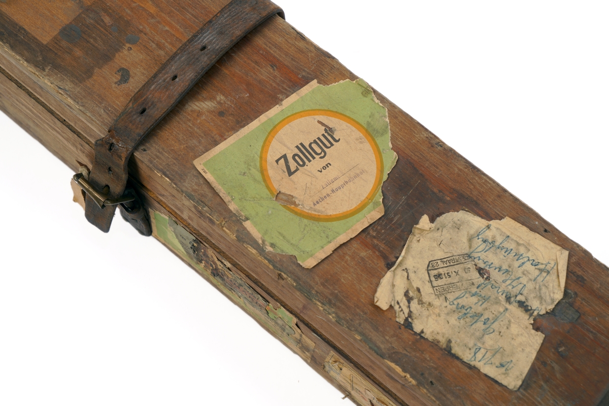 Trekasse med låsbart, hengslet lokk. Nøkkel mangler. Kassen er forsterket med metallbeslag. Lokket kan også låses med to påskrudde lærreimer med spenner. Nøkkelhullet er forsterket med metallbeslag.