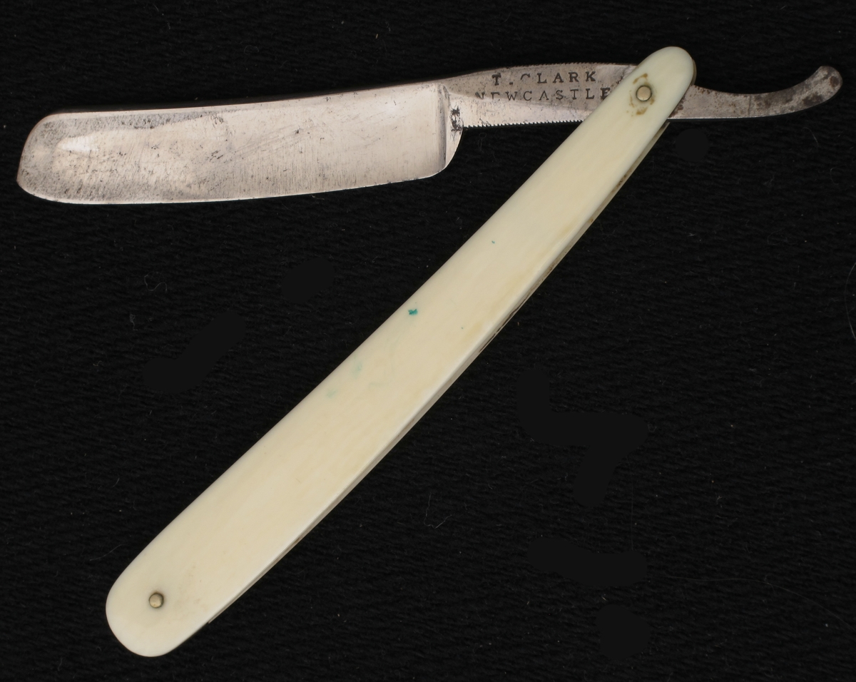 Barberkniv i futteral.  Stållblad st.: T. Clark Newcastle, benskaft.  
Sort pappfutteral med firmanavn. trukket med lær.