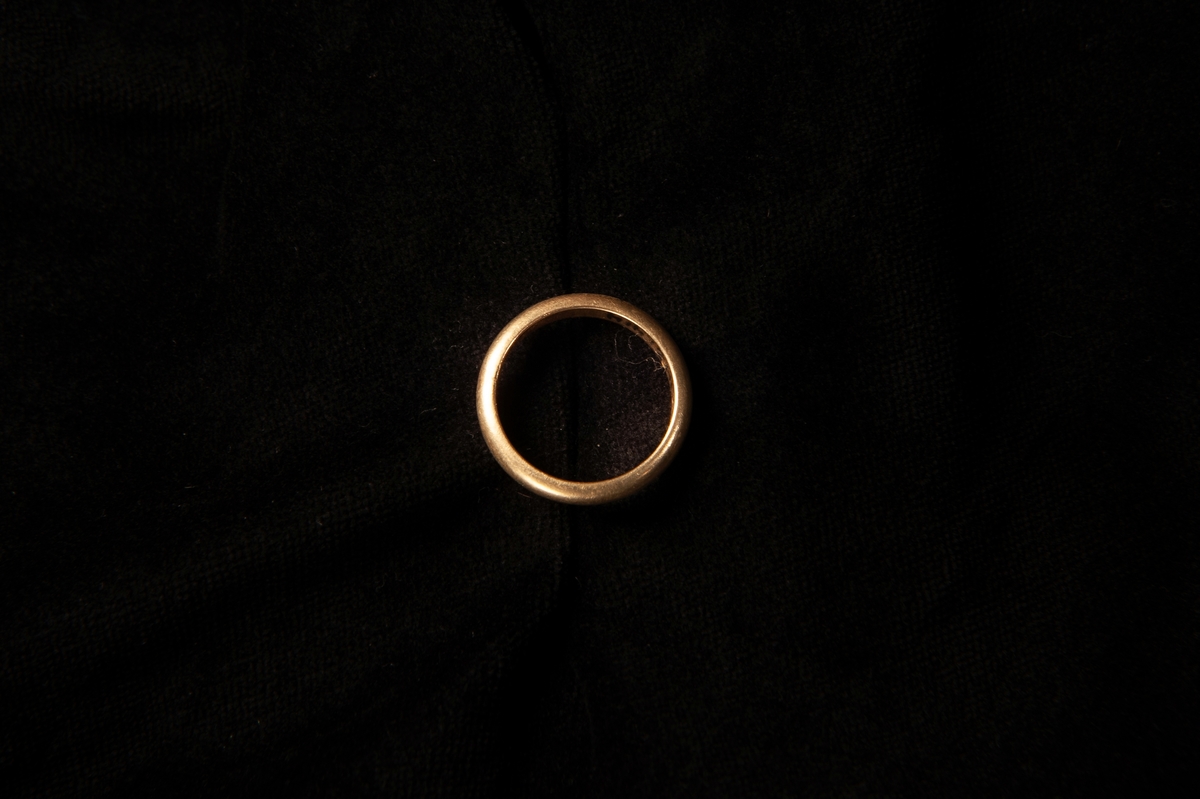 Fingerring av gulddouble, liggandes i en rund smyckesask med lock. Asken har ett marmorerat mönster, svart med roströd botten. Locket är rostrött med små inpräglade streck. Eventuellt hör inte de olika askdelarna till varandra från början.