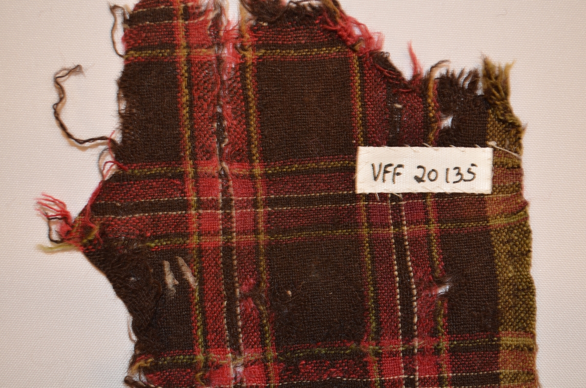 Stoffbit i ull, rutete i sauebrunt, raudrosa, kvitt grønt.