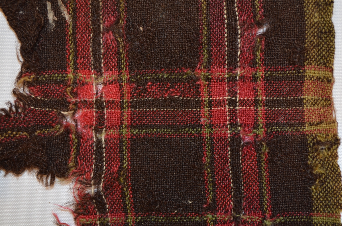Stoffbit i ull, rutete i sauebrunt, raudrosa, kvitt grønt.