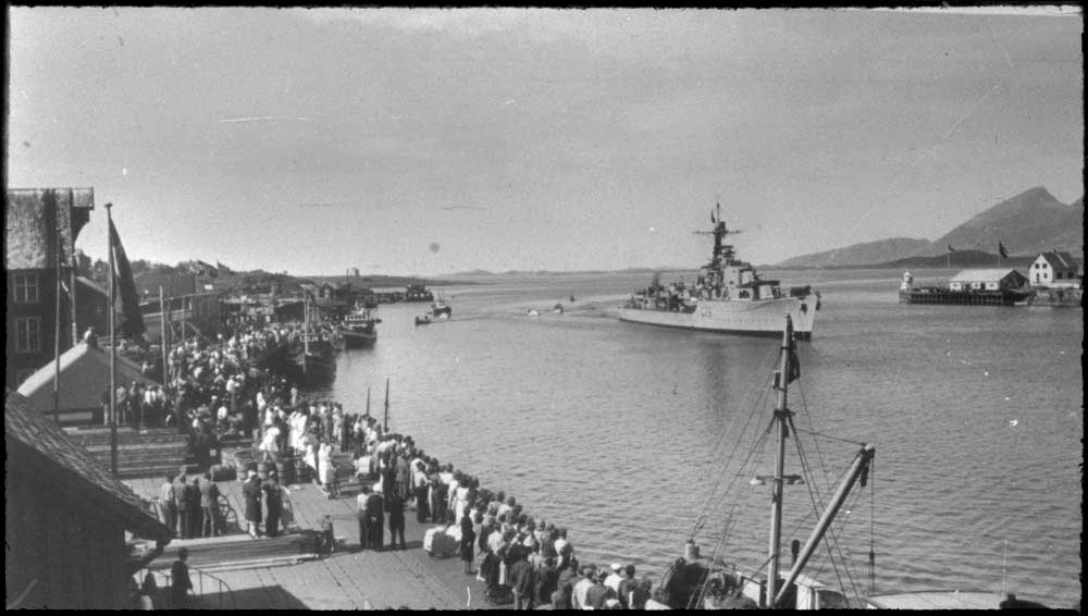 Sandnessjøen, Havna. Marinefartøyet på bildet er jageren KNM Stord G26. Skipet førte Kong Haakon på rundreise i Nord-Norge, og fører kongeflagget i formasten. Underveis til Mo i Rana, passerte skipet Sandnessjøen i sakte fart og hilste de frammøtte på kaien.