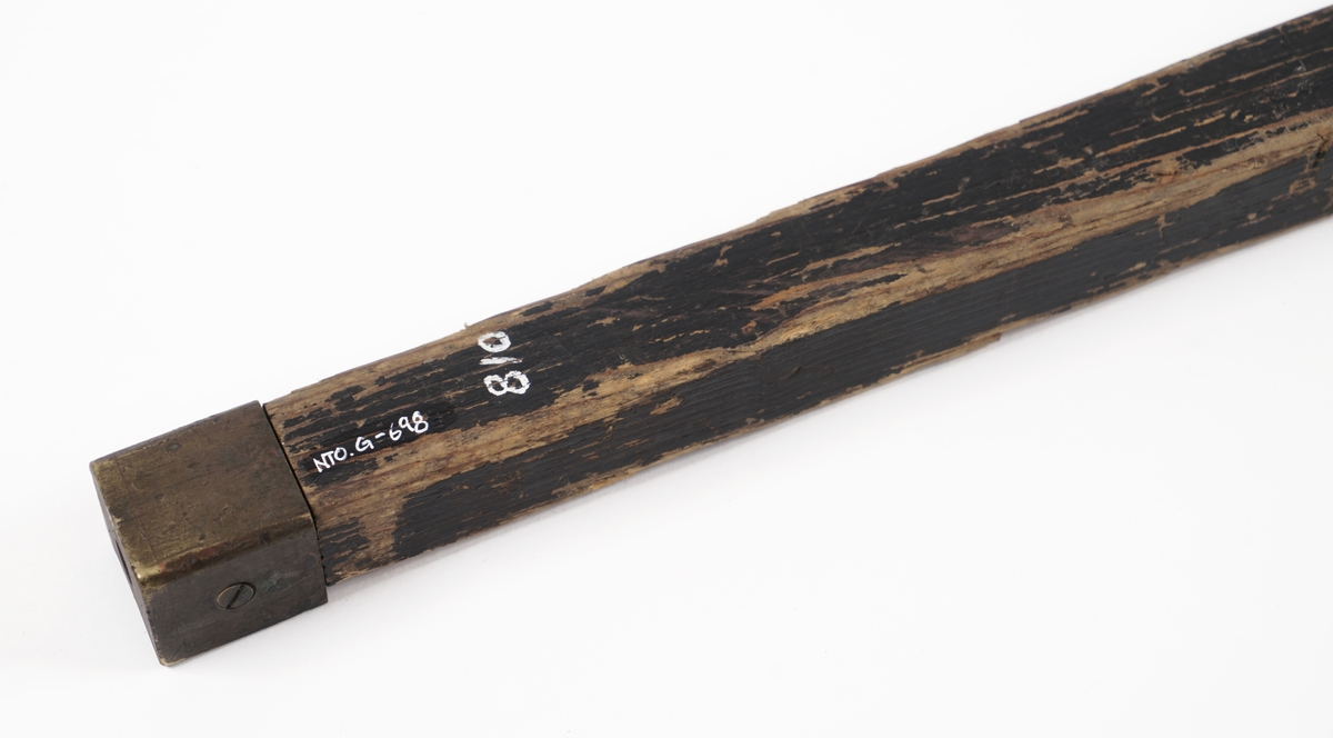 Lengdemål av tre. Sortmalt.Målsiden er konkav.Messingbeslag i begge ender