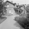 Åkers styckebruk stationshus ur  trägårds synvinkel.  I vänster kanten skymtar en buss med  passagerare. Stationen uppfördes 1895. Bangården ombyggdes 1947 med bredare plattformar och längre spår. I början av 1950 byggdes ett nytt stationshus.