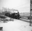 Statens Järnvägar SJ 1856-1956. 100-årsjubileum. Tåg med gamla lok och vagnar vid Tegelbacken på väg mot Stockholm Central, på sträckan mellan Riddarholmen och Stockholm Central. Bergslagens Järnvägar BJ K 27.