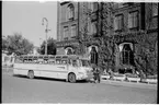 Statens Järnvägar, SJ Turistbuss med förare och värdinna, här utanför Malmö centralstation.
Bussen på bilden tillverkningsnummer 2284. Den ingick i en serie bussar av typ Scania-Vabis B 63 special från 1954 med Hägglundskaross från Örnsköldsvik, omfattade serien 2279-2288.
Dessa var utrustade med lyxinredning, toalett, kylskåp och bussvärdinna. Vid varje sittplats fanns en knapp som resenären kunde trycka på, varvid det då hos bussvärdinnan i bakre delen av delen i bussen, en liten plåtbrickaföll ner med sittplatsnummer så vederbörande direkt kunde uppsöka rätt plats. Dessa bussar var avsedda enbart för utlandstrafik eftersom in/utgång fanns på bussens bakgavel.
Buss 2285 av exakt samma typ finns bevarad hos 
Helsingborgstrafikens museiförening.
PÖ