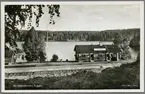 Ryggen station sedd från spårsidan med Ryggen sjön i bakgrunden.