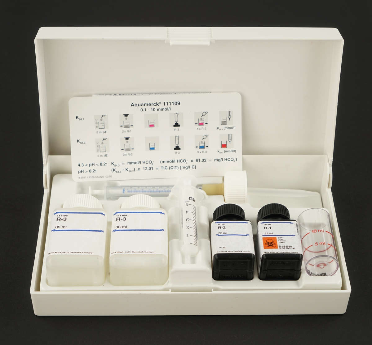 Plastboks med lokk inneholdende  fire plastflasker med skrukork med kjemikalier, ett målebeger, en sprøyte og en pipette, samt to typer bruksanvisning.