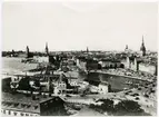 Statens Järnvägar, SJ, Stockholm utsikt från Katarinahissen 1930, innan slussbygget påbörjades och hissen rivits. Denna utsikt är numera historiskt. (bilden köpt 1935 från Svenska Turistföreningen.) Gamla riksdagshuset flygel mot Mälaren påbyggd och fullbordad år 1908 efter ritningar av Aron Jonsson. Uppgift från Stadsmuseets bildarkiv. 1956 06 12. Södra slöjdmagasinet och Mazettie ligger till höger om järnvägen.