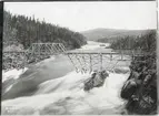Provisorisk bro över Stora Luleälven alldeles ovanför den järnvägsbro som höll på att byggas längs Inlandsbanan. I bakgrunden skymtar Porjusberget.