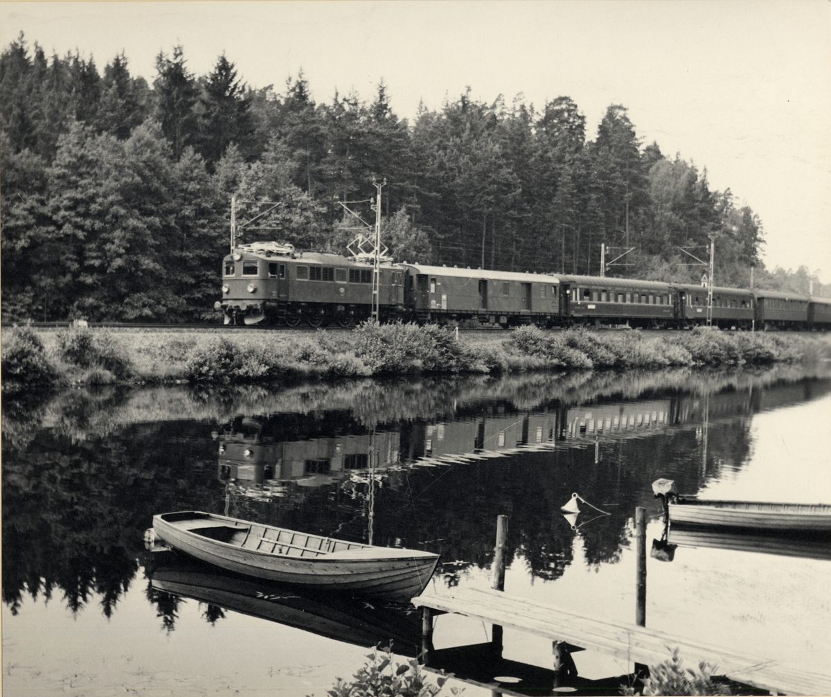 F-lok med svenska och tyska vagnar kör längs med en sjö eller älv med småbåtar.