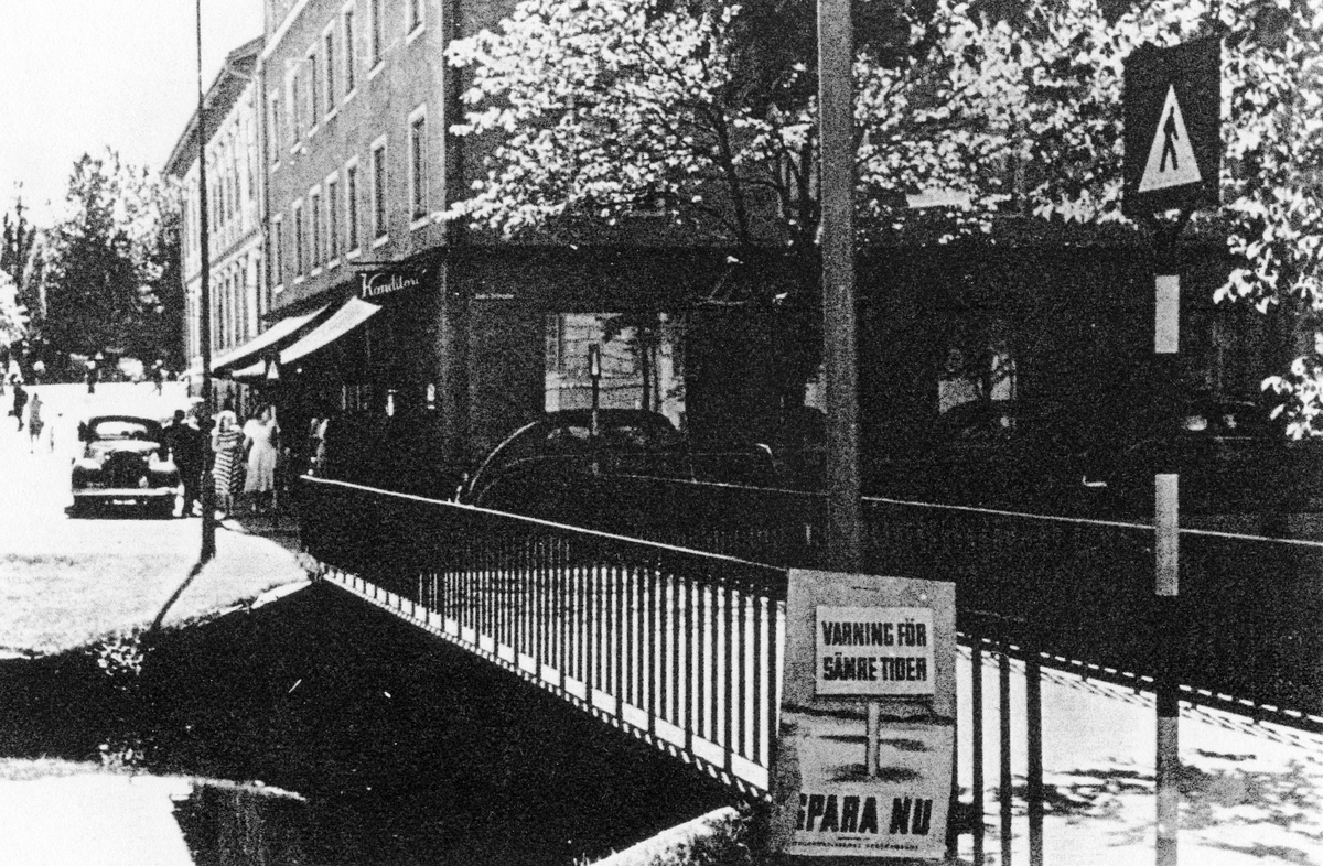 Gatuvy av Ljungblads konditori, främst på bilden en reklamskylt om sparande "Varning för sämre tider - Spara nu". 

Ljungblads konditori, Lilla torget 3, Kvarteret Pelikanen 2A. 
Konditoriet låg tidigare på Kungsgatan, kvarteret Hjorten.