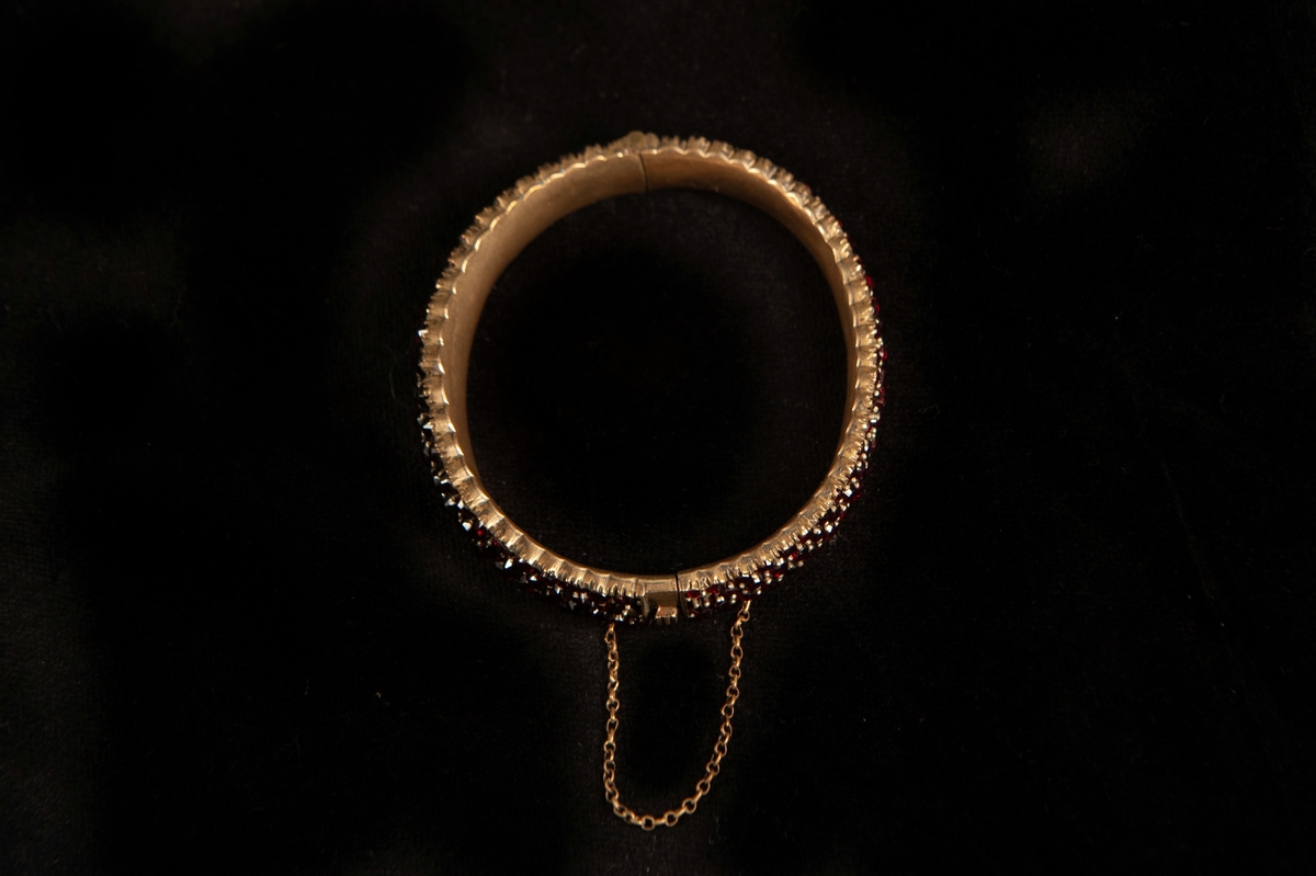 Ett armband, tätt besatt med slipade röda granater. Infattade i förgylld metall, troligen silver. Armbandet något avsmalnande åt sidorna.Smycket ligger i specialgjord svart, ask med röd sammet invändigt och ett snäpplås. 
Inga stämplar på armbandet.